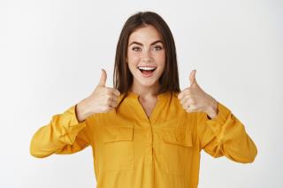 impressed-young-woman-showing-thumbs-up-smiling-amazed-praising-something-cool-standing-white-wall
